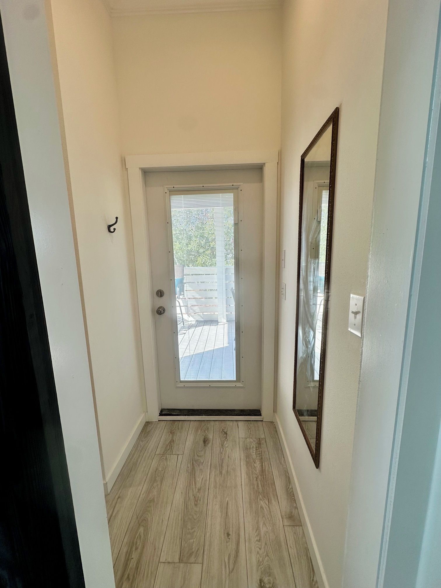 Un couloir étroit avec un plancher en bois, une porte blanche dotée d’une fenêtre et un miroir accroché au mur.
