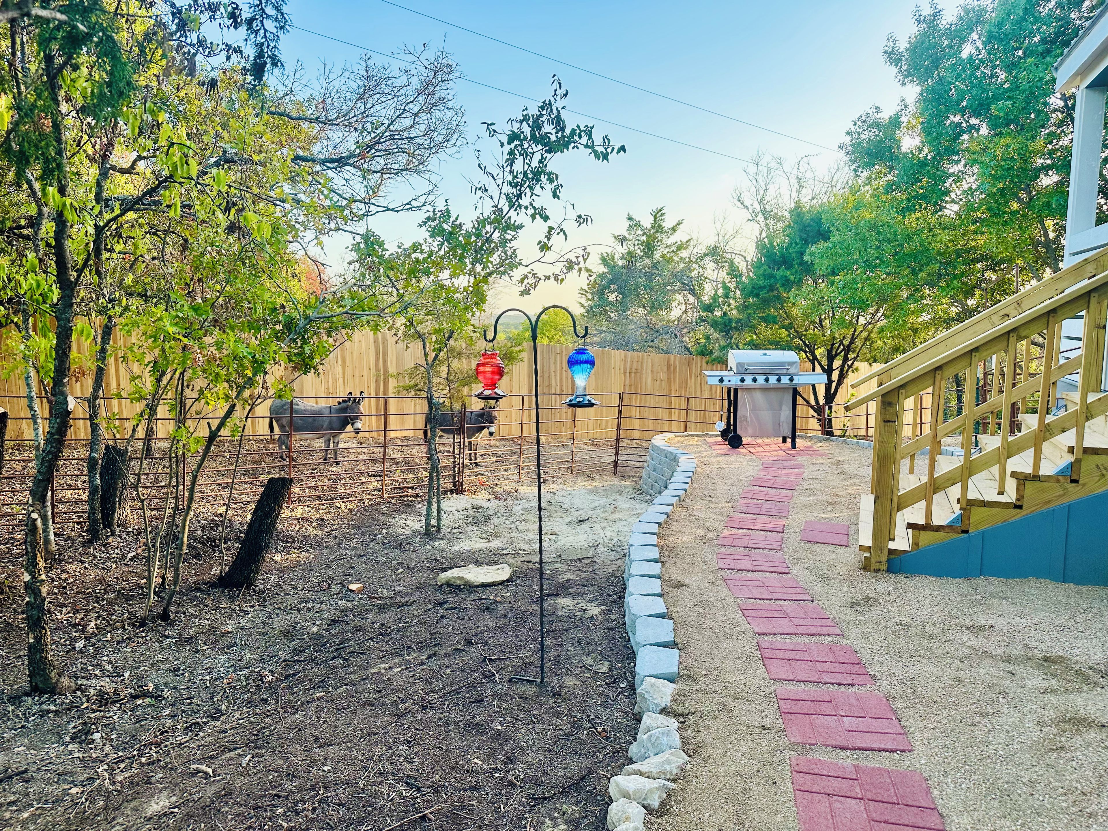 A fenced outdoor area with a barbecue grill, a wooden deck, and a brick pathway.