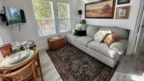 Ein Wohnzimmer mit einer Couch, einem Flachbildfernseher, einem Esstisch mit Tellern und einem gemusterten Teppich.