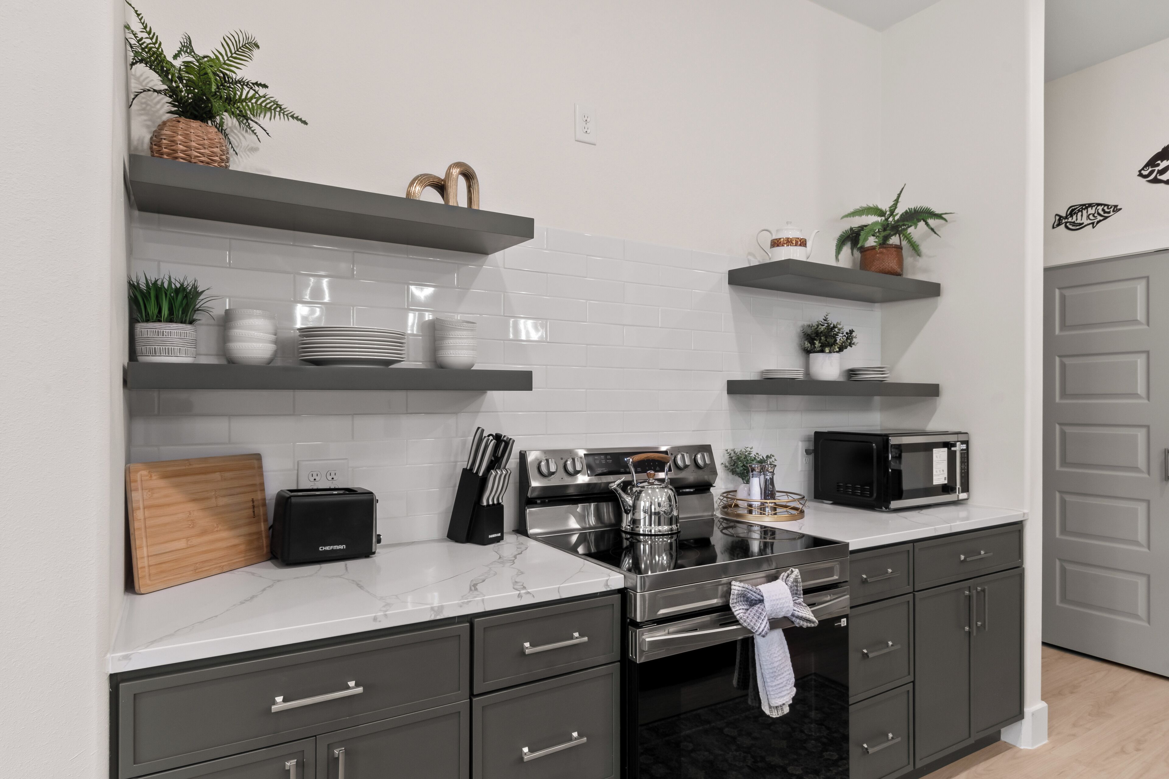 A modern kitchen with grey cabinets, a stainless steel stove, a microwave, and various kitchen utensils.