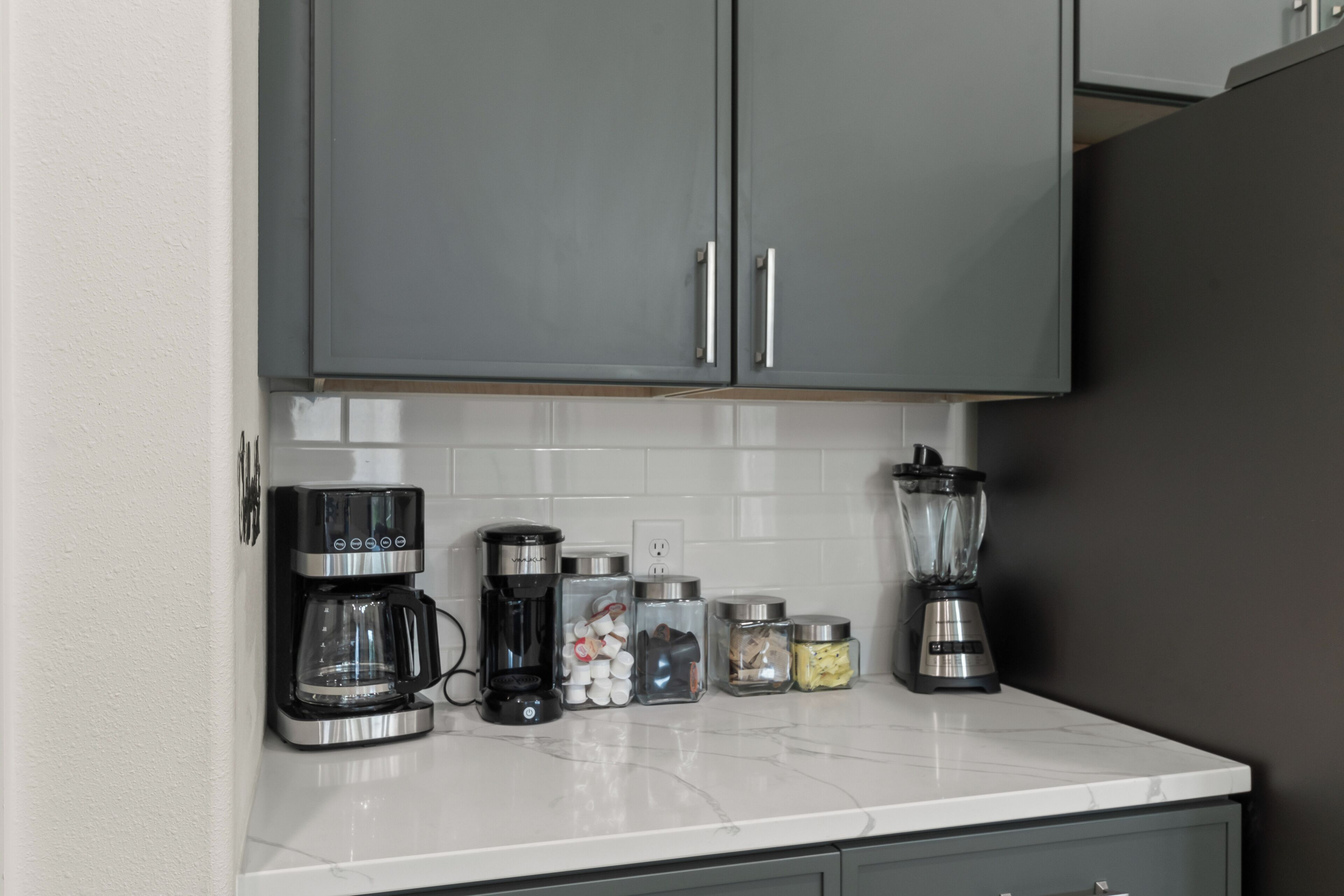A kitchen with a coffee maker, a blender, and storage jars on the counter.