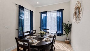 A dining room with a round table, chairs, a potted plant, and curtains.