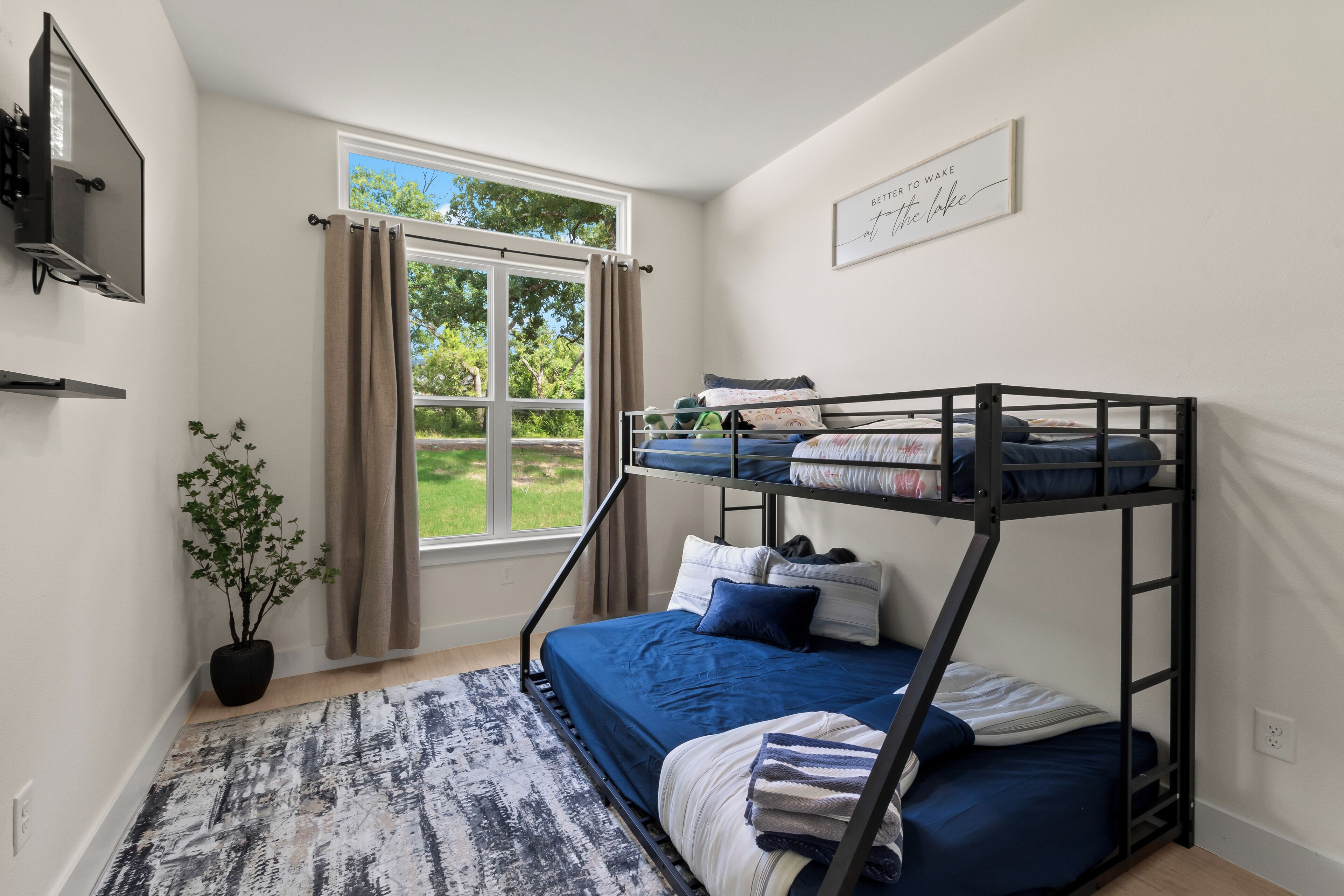 Habitación con literas, ventana, planta en maceta y televisor montado en la pared.