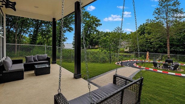 A covered outdoor seating area with swings, a view of a landscaped park, and a fenced pathway.