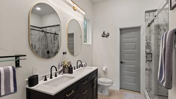 A modern bathroom with a double sink vanity, a toilet, and a shower area.