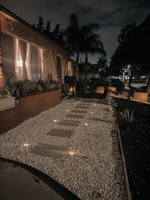A nighttime outdoor pathway with stepping stones, surrounded by plants and a building with illuminated windows. - Quiet Lakewood Gem. A Charming 3-bedroom Home away from Home (Lakewood)