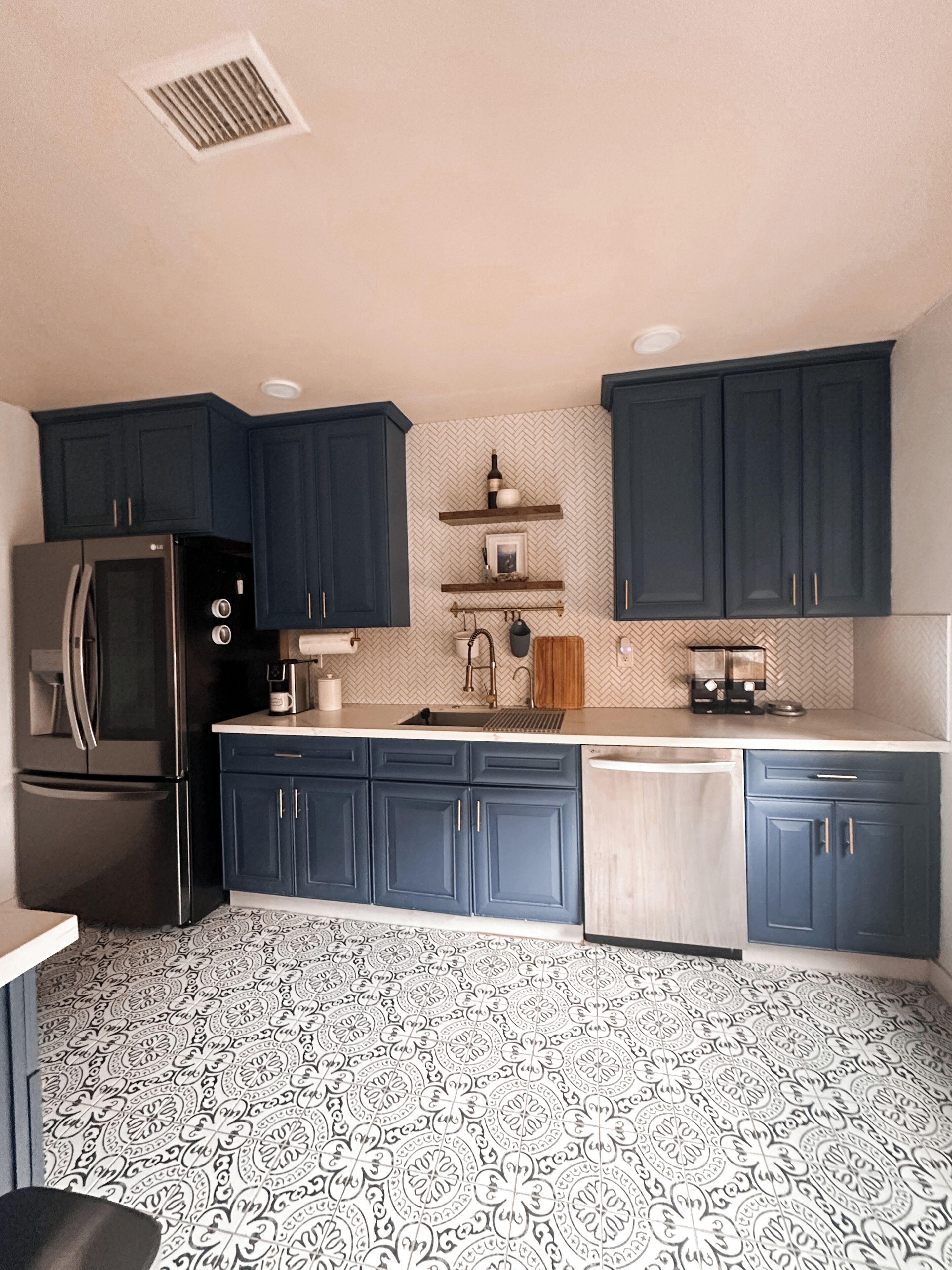 A kitchen with dark blue cabinets, a stainless steel refrigerator, and patterned floor tiles.