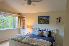 Ein Schlafzimmer mit Bett, Deckenventilator, Fenster mit Jalousien, einem Gemälde und einem Nachttisch mit Lampe.