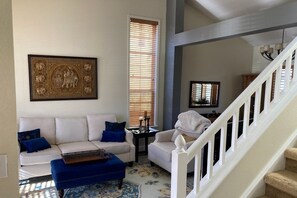 A living room with a white sofa, blue cushions, a blue ottoman, a framed artwork, and a staircase. - Eco-friendly 4-bedroom Louisville Sanctuary Near Trails (Louisville)