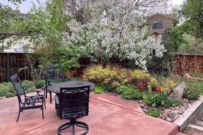 An outdoor patio with a round table and chairs, surrounded by a garden with various plants and a flowering tree. - Eco-friendly 4-bedroom Louisville Sanctuary Near Trails (Louisville)