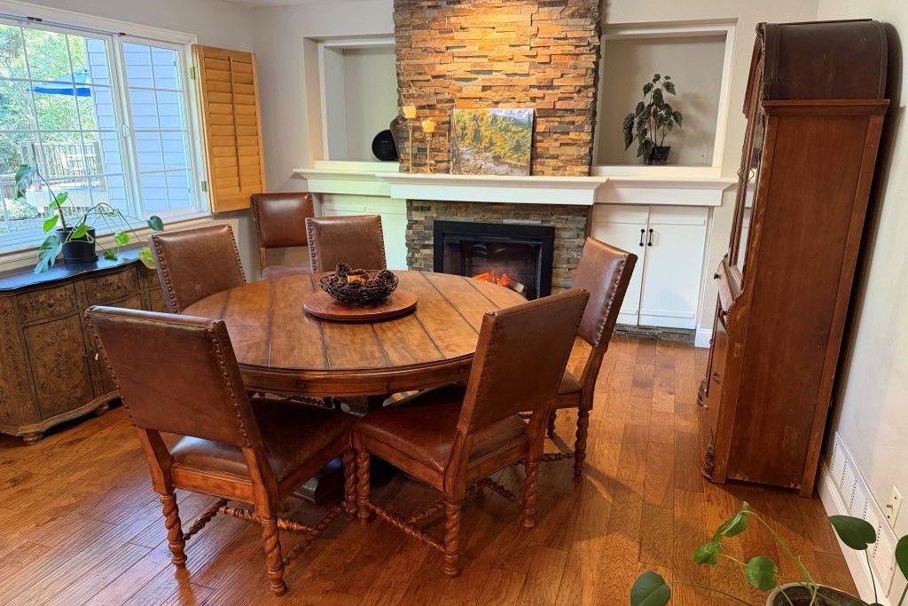 A dining room with a round wooden table surrounded by six chairs, a fireplace, and a stone accent wall.