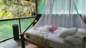Un letto a baldacchino, una panca di legno e vista sulla vegetazione attraverso una zanzariera.