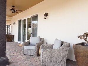 A covered patio area with wicker furniture, a ceiling fan, and a potted plant.