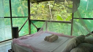 A bed with a mosquito net, a rolled towel, and a view of greenery through the window. - Río Agujitas Rainforest Eco Lodge - Habitación Doble Estándar (Agujitas (Drake))