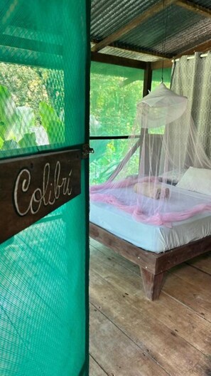 Un letto con zanzariera, pavimento in legno e un cartello con scritto 'Colibri'.