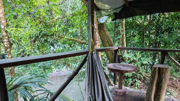 A wooden deck with a hammock, a small round table, and a rustic bench, surrounded by dense tropical foliage. - Río Agujitas Rainforest Eco Lodge - Habitación Doble Deluxe (Agujitas (Drake))
