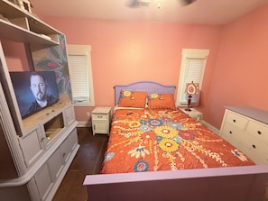 Quarto com cama, televisão, penteadeira e mesa de cabeceira.
