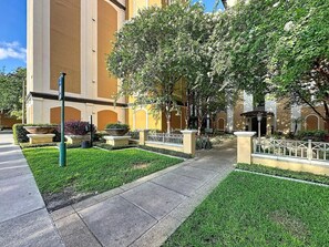 Une cour avec un chemin pavé, une fontaine et un bâtiment à la façade jaune.