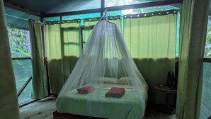 Una cama con mosquitero, una mesita pequeña y una ventana con cortinas.