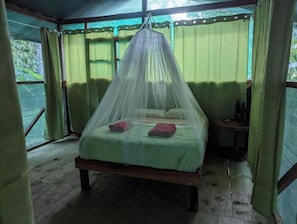 Un lit doté d’une moustiquaire, une petite table et une fenêtre avec des rideaux.