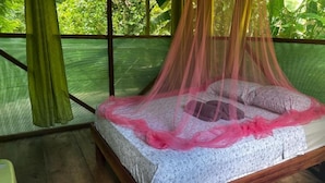A bed with a canopy, surrounded by a mesh screen, and a green curtain. - Río Agujitas Rainforest Eco Lodge - Habitación Cuádruple Deluxe (Agujitas (Drake))