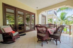 A covered outdoor area with wicker furniture, a dining table, and a view of palm trees and a pool. - Salty Breeze Suite|Seaview Family Residence w/Pool (San Pedro)