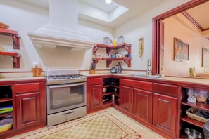 Une cuisine équipée d’une cuisinière, d’un four et de meubles de rangement rouges. On y trouve des étagères remplies d’ustensiles de cuisine et une fenêtre au-dessus de l’évier.