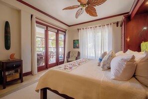 Une chambre à coucher avec un lit, un ventilateur de plafond, une table de chevet, une fenêtre avec des rideaux et une vue sur l’extérieur.