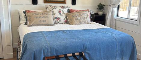 A bedroom with a bed, a wooden bench, a patterned rug, a ceiling fan, and a window with curtains.