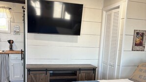 Un dormitorio con una cama, un televisor montado en la pared, un armario de madera y una puerta con ventanal.