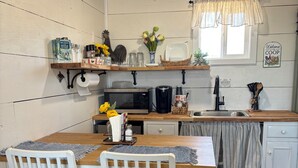 Una cocina con encimera de madera, armarios blancos, una mesa de comedor con sillas y una ventana con cortinas.