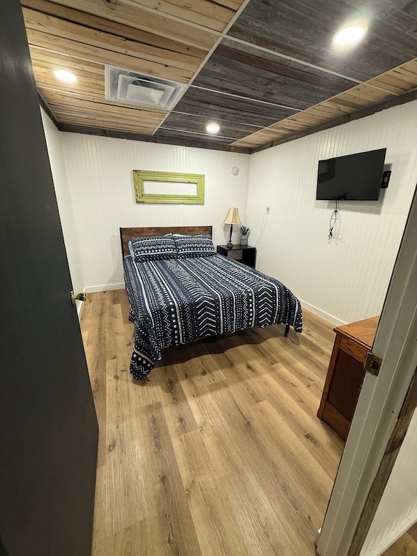 A bedroom with a bed, a TV mounted on the wall, and a wooden ceiling.
