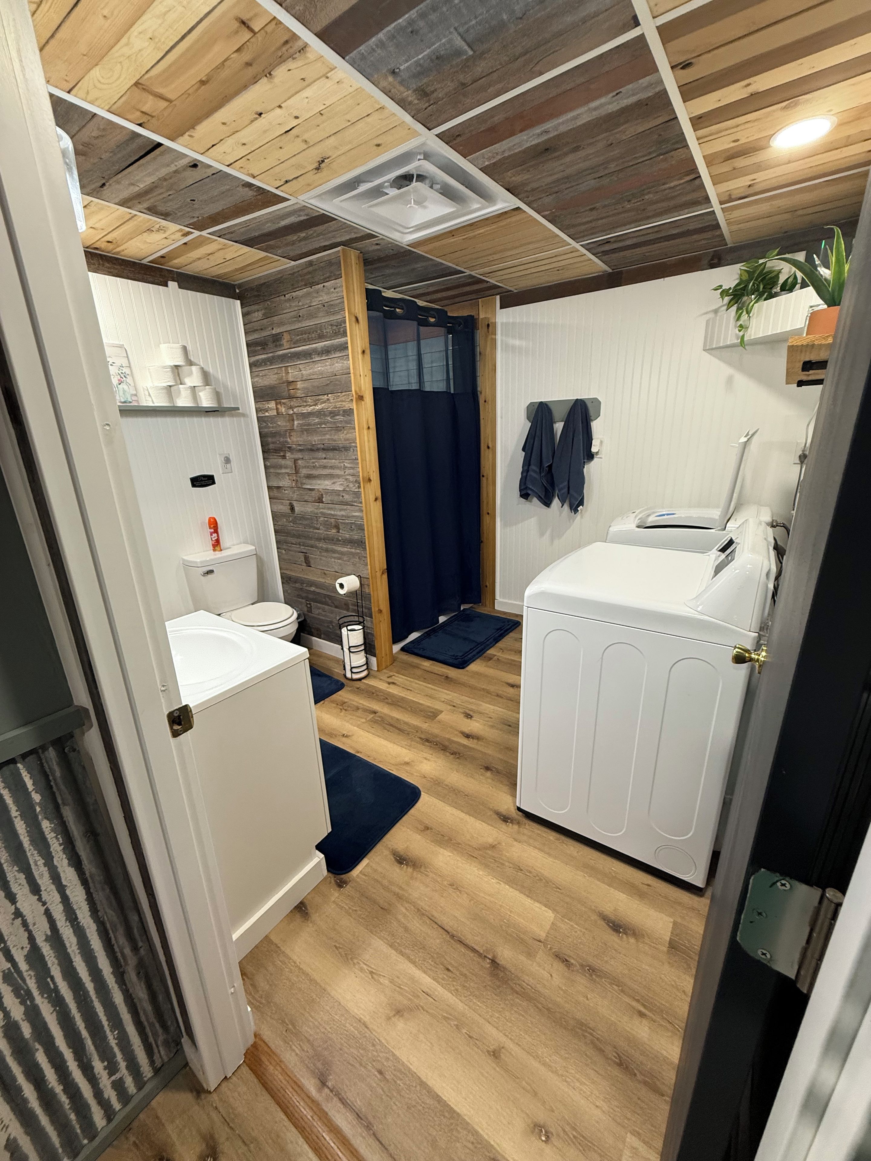 Une pièce de taille modeste avec un plafond en bois, un radiateur blanc, un petit lavabo, des toilettes et un lave-linge.