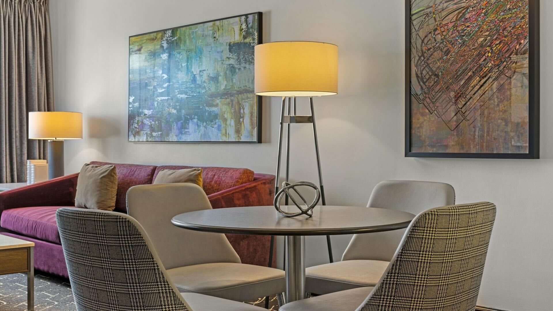 Habitación de hotel con una mesa redonda, dos sillas, un sofá y dos lámparas de pie.