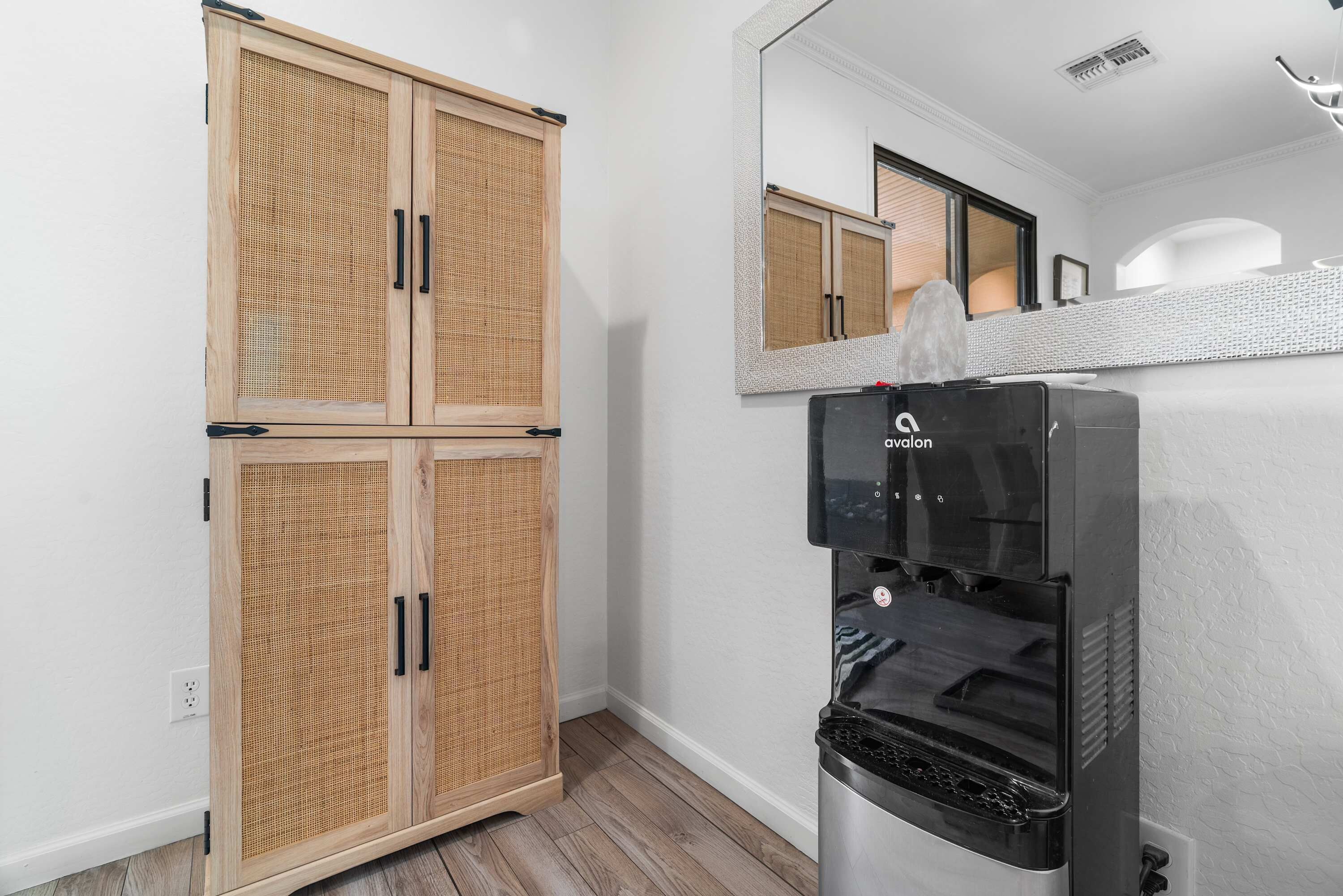 A room with a wooden wardrobe, a water dispenser, a mirror, and a white wall.