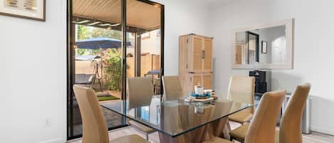Un comedor moderno con una mesa de vidrio rodeada de sillas de cuero, un armario de madera y una zona de cocina con dispensador de agua.