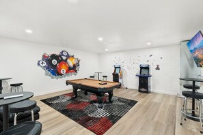 Ein Billardtisch in einem Raum mit weißer Ziegelwand, einem Billardtisch und zwei Spielautomaten.