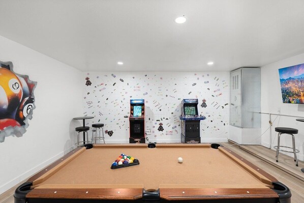 A pool table with a pool cue and balls, arcade machines, and a mural with various icons. - The Desert Palm! Private Oasis! Heated Pool (Glendale)