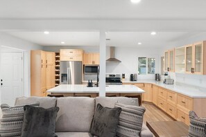 Eine moderne Küche mit Kochinsel, Holzschränken, Edelstahlgeräten und einer Sitzecke inklusive Sofa und Kissen.