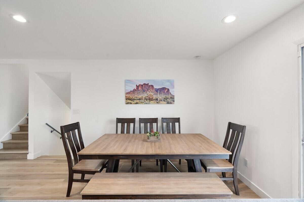 A dining area with a wooden table and chairs, a staircase in the background, and a painting on the wall.
