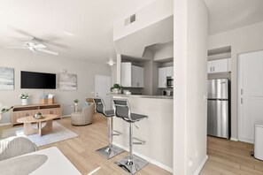 Een moderne keuken met roestvrijstalen apparatuur, een bar met barkrukken en een eethoek met een houten tafel en stoelen.