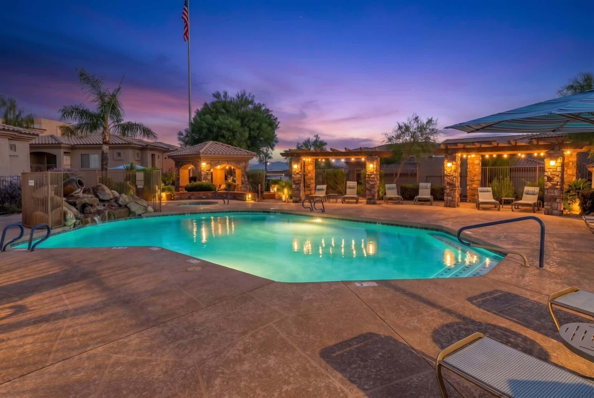A swimming pool with lounge chairs and a stone structure with lights.