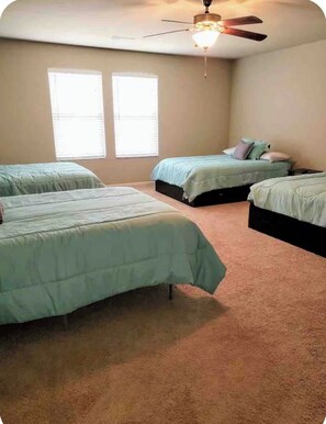 A bedroom with two beds, a ceiling fan, and two windows.