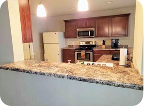A kitchen with granite countertops, a stainless steel microwave, a stove, and wooden cabinets.