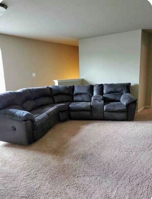A sectional sofa in a living room with a carpeted floor and a plain wall.