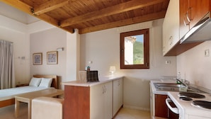 A compact bedroom with a bed, bedside table, and a small sitting area. A kitchenette with a stove, sink, and cabinets is adjacent to the bedroom. - Villa 'Kalirroe' in Marathiás (Marathiás)
