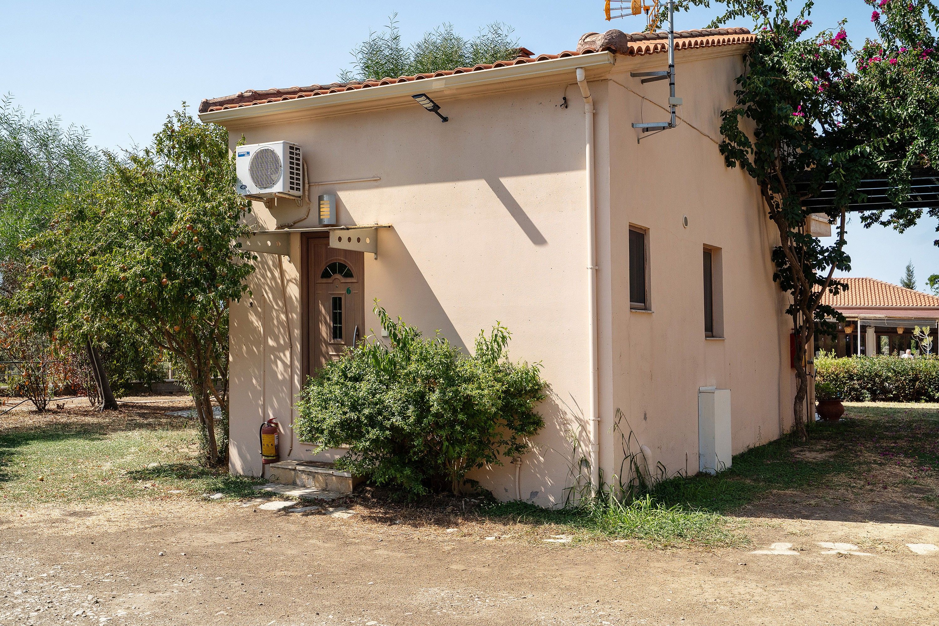 A small building with a beige exterior, a tiled roof, and an air conditioning unit mounted on the wall.