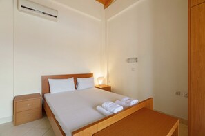 Habitación de hotel con una cama individual, una mesita de noche, un banco de madera, un equipo de aire acondicionado y un enchufe de pared.