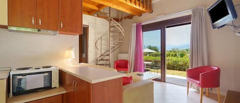 A compact kitchen with wooden cabinets and a built-in stove, a dining area with a table and chairs, and a balcony with a TV and a view of the landscape.