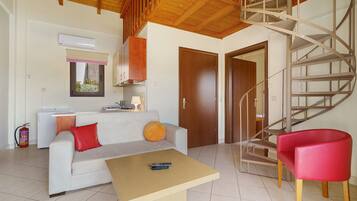 Un espacio habitable compacto con sofá, una mesita, una silla roja, una escalera de madera y una puerta que da a otra habitación.
